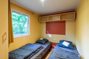 A room with two single beds, a window with curtains, a red wall, and built-in shelving above the beds.