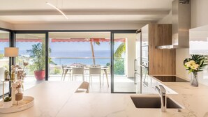 A modern kitchen with a view of the ocean, a dining area with a table and chairs, and a large potted plant. - Florida Soleil luxury and sea view (Schoelcher)