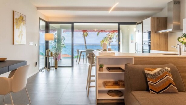 A modern living room with a sofa, a dining area, and a kitchen. There is a large window with a view of the ocean. - Florida Soleil luxury and sea view (Schoelcher)