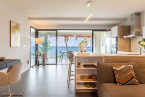 Un saló modern amb un sofà, una zona de menjador i una cuina. Hi ha una finestra gran amb vistes a l'oceà.