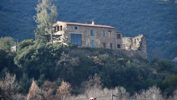 Un edificio de piedra con techo de tejas rojas, ubicado en una ladera con vegetación densa.