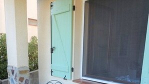 Un patio con pared de piedra, una mesa verde, dos sillas y una ventana con persiana cerrada.