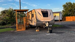 A recreational vehicle (RV) parked on a gravel surface with a wooden deck and a small porch. - Starlight Retreat RV in Springtown with AC, WiFi (Springtown)