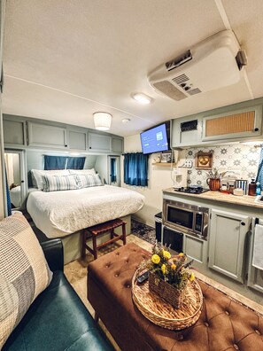 A compact RV interior with a bed, kitchenette, and seating area. - Starlight Retreat RV in Springtown with AC, WiFi (Springtown)