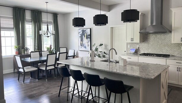 Una cocina moderna con una isla central, taburetes de bar, luces colgantes y un comedor con mesa y sillas.