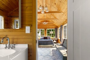 L’intérieur d’un chalet en bois comprend une salle de bain, une chambre avec un lit et une fenêtre, ainsi qu’un coin salon.