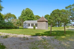 Eine kleine Holzhütte mit spitzer Dachform, umgeben von einer Wiese und Bäumen.