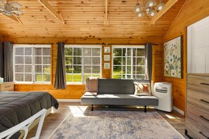 Een gezellige slaapkamer met een bed, een slaapbank, een verwarming en grote ramen met uitzicht op het omliggende landschap.