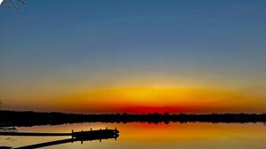 A calm lake at sunset with a dock extending into the water. - Escape to a cozy château in Lambert’s Cove, Stonington, CT. (Stonington)