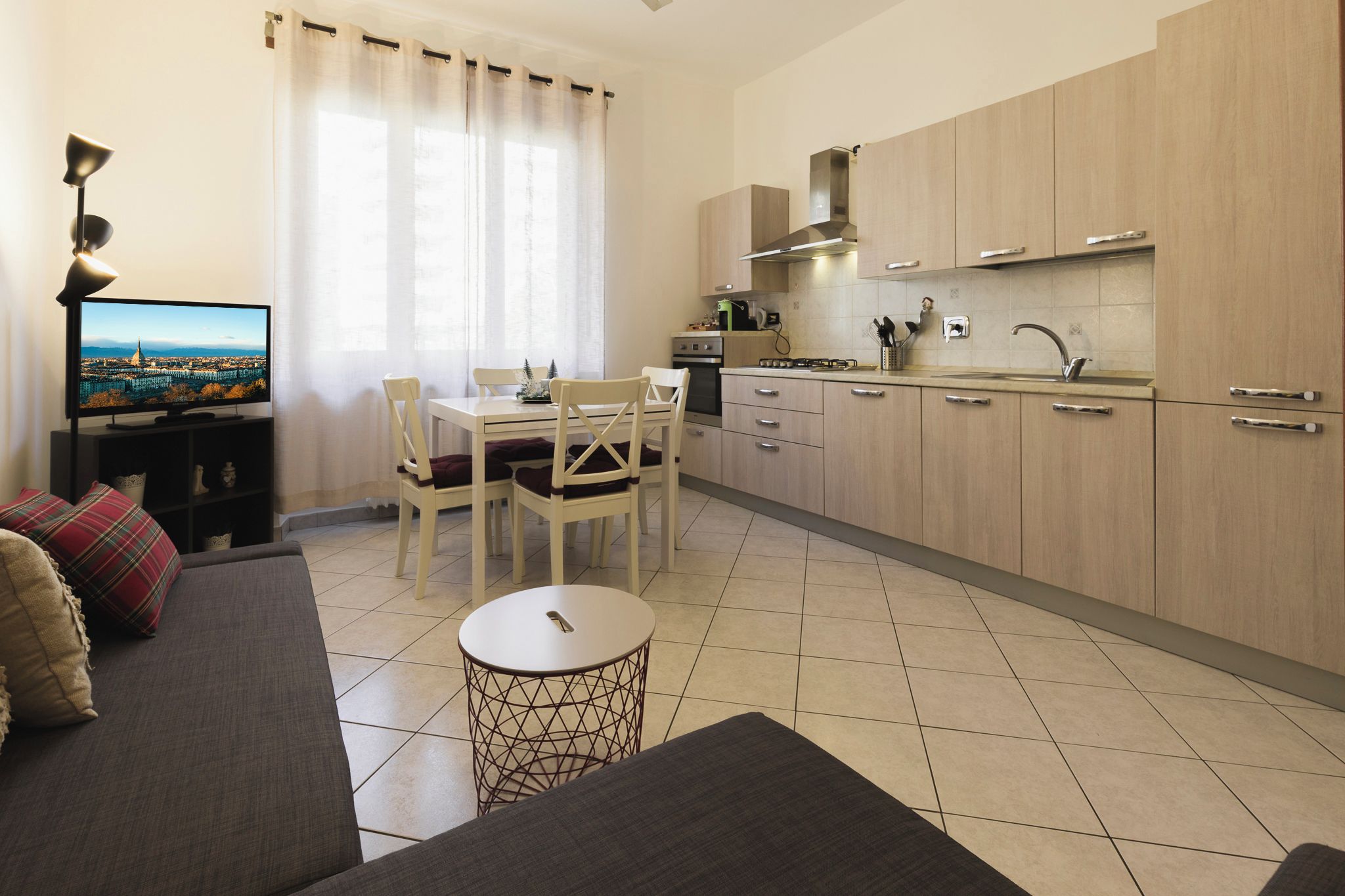 Un soggiorno moderno con divano, televisione, tavolo da pranzo con sedie e angolo cottura con pensili e piano cottura.