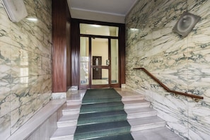 A marble staircase with a wooden handrail leading to a door with glass panels.