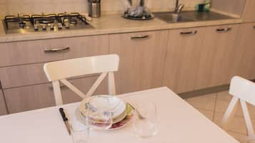 Una cucina con gas, lavello e pensili. Si nota un tavolo da pranzo con piatti, bicchieri e posate.