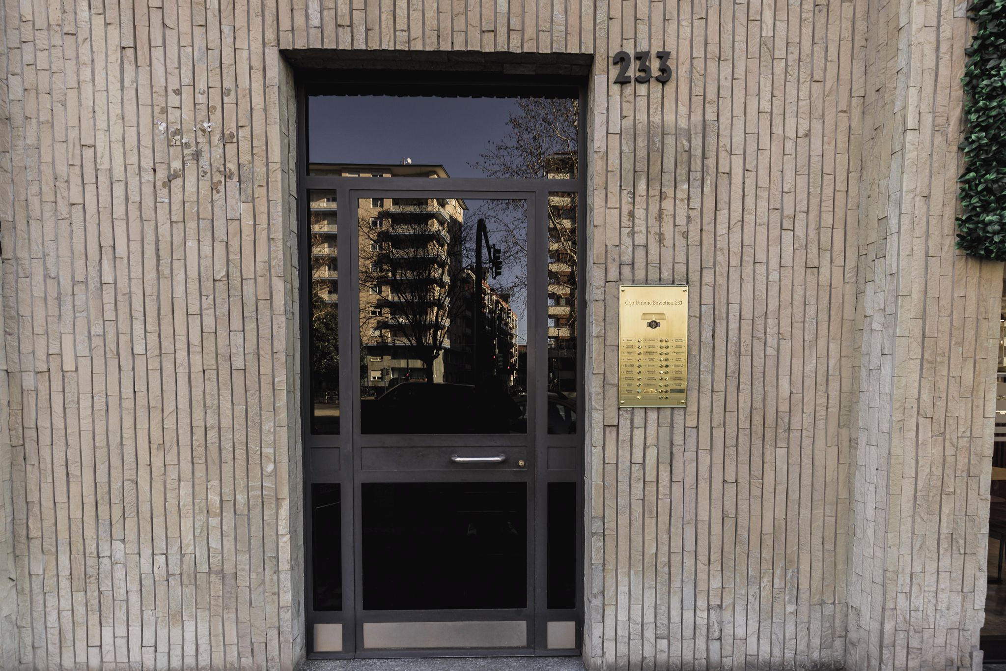 Ingresso di un edificio con una porta numerata, una tastierina e il riflesso di grattacieli.