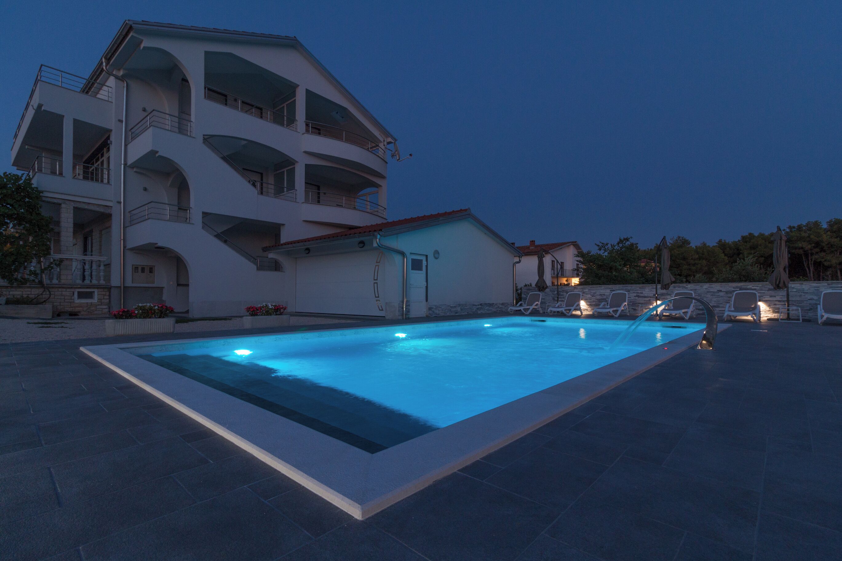 Un bâtiment moderne doté d’une piscine, d’un espace extérieur aménagé et d’une petite structure adjacente.