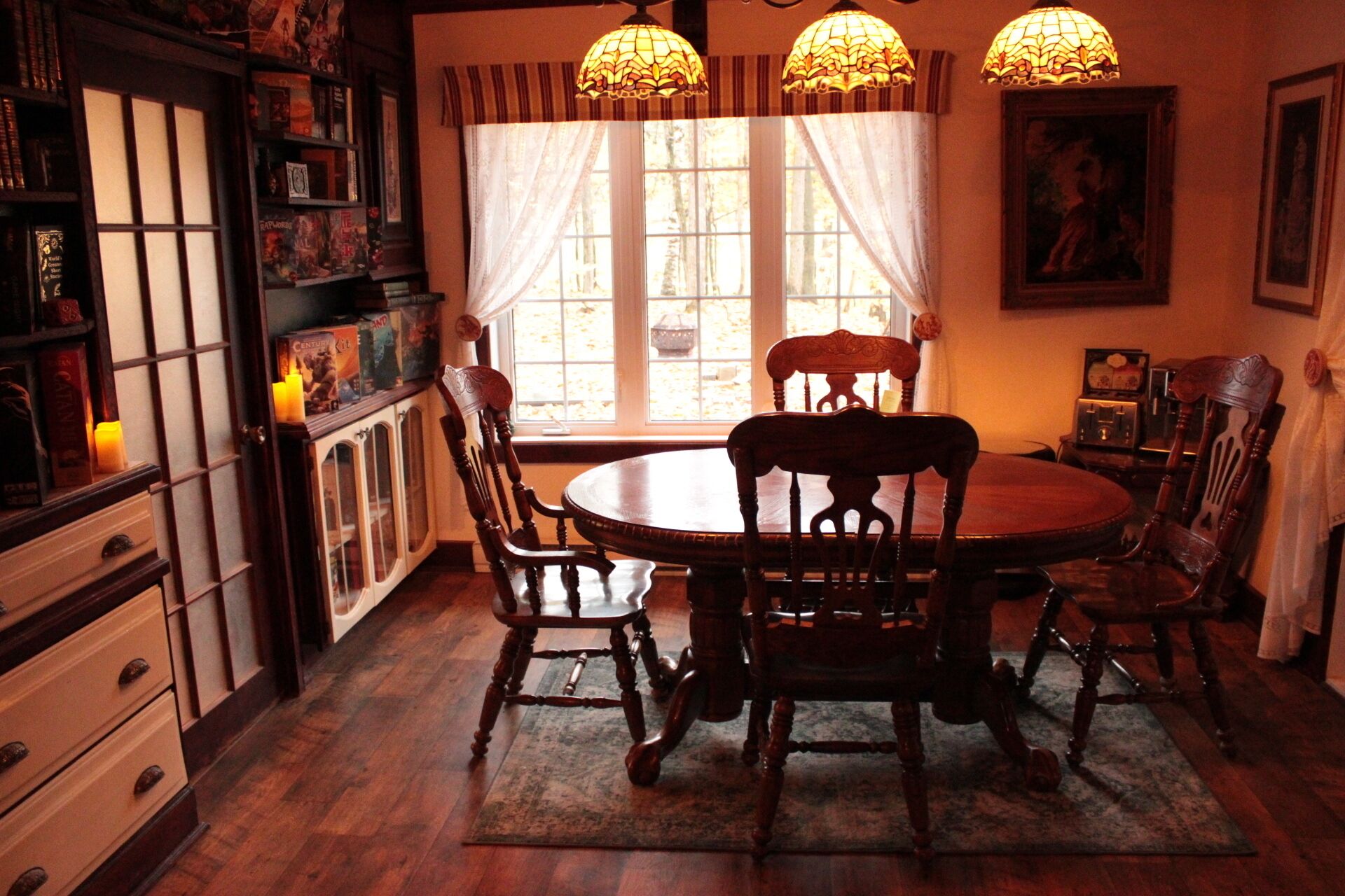 Un comedor con una mesa y sillas de madera, un aparador con puertas de vidrio y una ventana con cortinas.