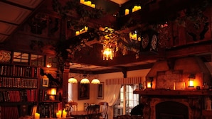 Una biblioteca cálidamente iluminada con estanterías, chimenea y plantas colgantes.