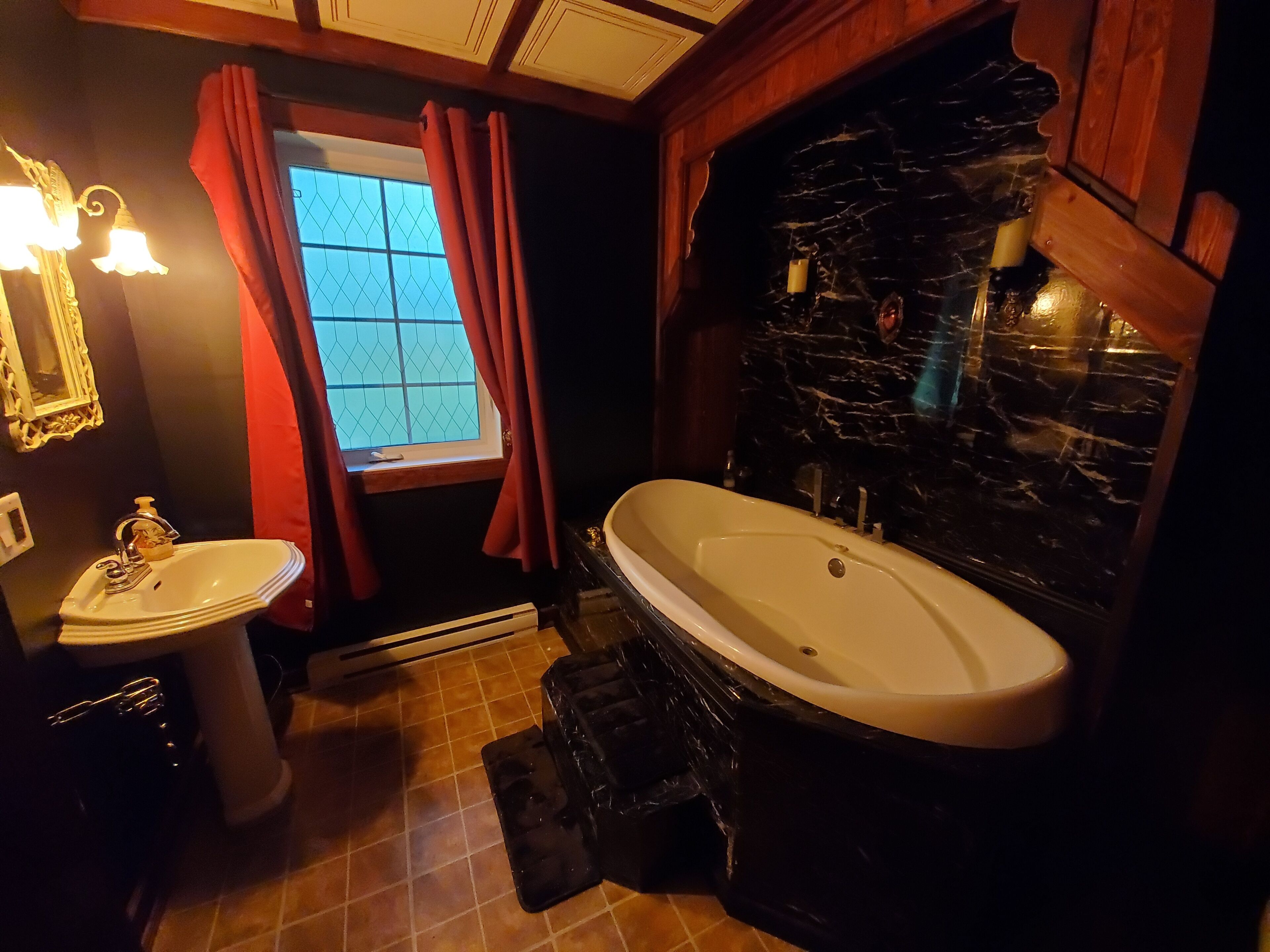 Une salle de bain avec un lavabo blanc, une baignoire et une fenêtre avec des rideaux rouges.