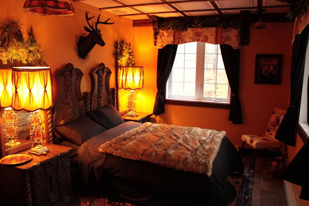 A cozy room with a bed, two lamps, a deer head on the wall, and a window with curtains.
