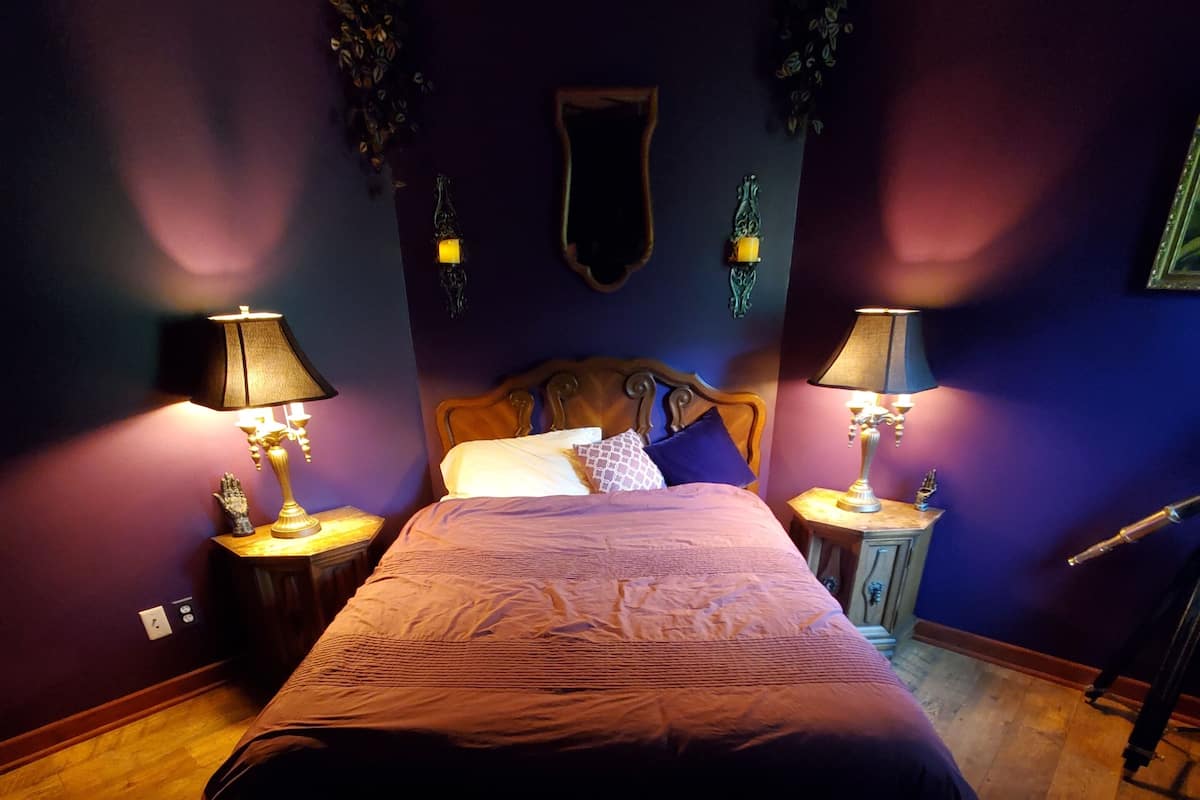 A bedroom with a wooden bed, two bedside tables with lamps, a mirror, and a wall-mounted decoration.