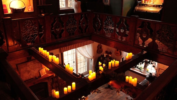 Una habitación tenuemente iluminada con una escalera de madera, varias velas y vistas a un nivel inferior.