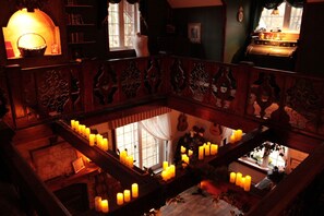 Una habitación tenuemente iluminada con una escalera de madera, varias velas y vistas a un nivel inferior.