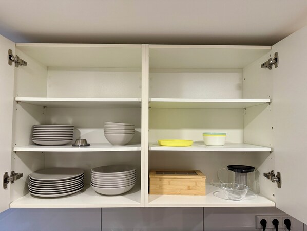 Un meuble de cuisine doté de plusieurs étagères, dont certaines contiennent des assiettes et des bols empilés, et d’autres abritent une boîte en bois et un récipient en verre.