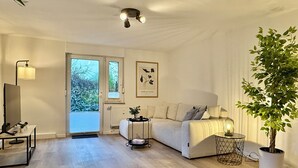 A modern living room with a sofa, a TV, a plant, and a ceiling light fixture. - 5-7 persons, Wifi, terrace, new, near Nordpark and supermarkets BIELEFELD (Bielefeld)