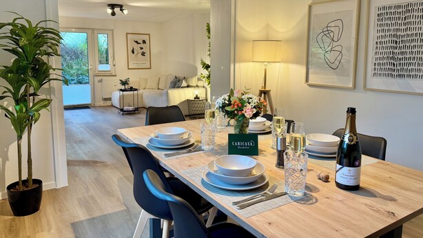 A dining area with a wooden table set for two, a bottle of champagne, and a floral centerpiece. - 5-7 persons, Wifi, terrace, new, near Nordpark and supermarkets BIELEFELD (Bielefeld)