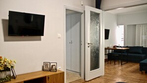 A modern living room with a flat-screen TV, a wooden console table with pictures, a dining area with a table and chairs, and a dark green sofa. - Apollo & Nike 1952-2025
Stylish 2-Bedroom apartment next to Syndagma Square (Athina)