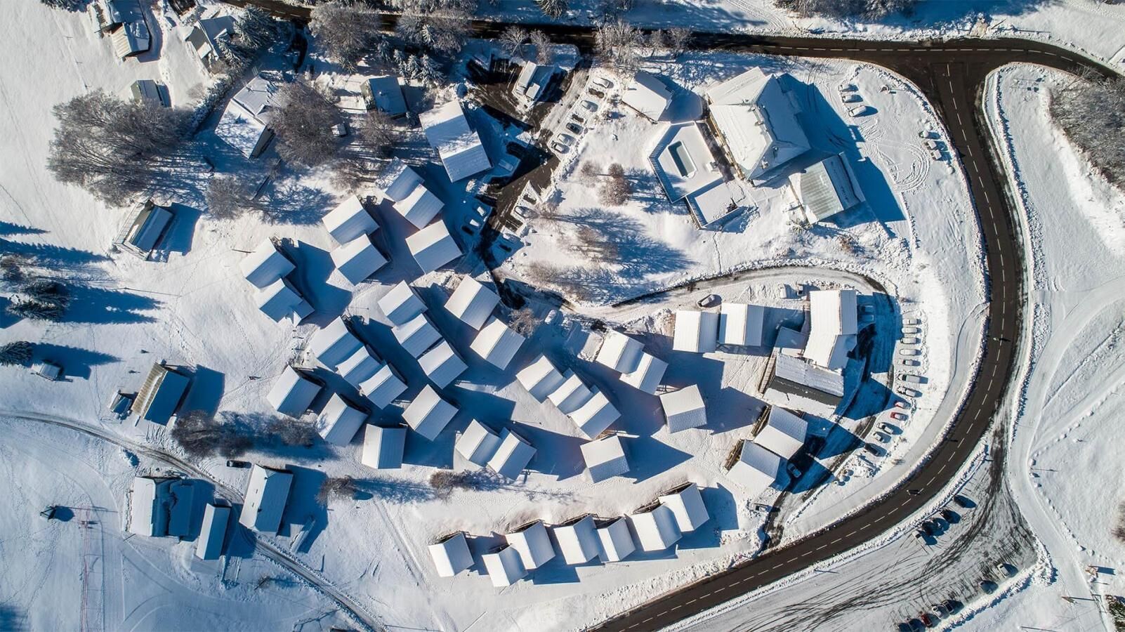 An aerial view of a snow-covered area with multiple buildings, roads, and parking spaces.