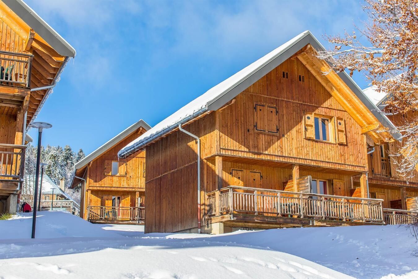 A wooden chalet with a balcony and a covered porch, surrounded by snow.