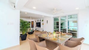 A modern dining area with a glass table, wicker chairs, and a large window.