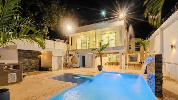 Una casa moderna con piscina, mobiliario exterior y un patio bien iluminado.