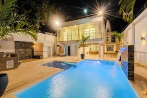 A modern house with a swimming pool, outdoor seating, and a well-lit patio area.