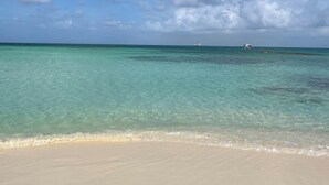 A beach with clear turquoise water, a sandy shore, and a distant boat. - 7-min Walk to Beach, King Bed, Jacuzzi Costa Caribe Studio (Noord)