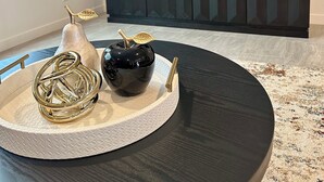 Una sala moderna con una mesa de comedor redonda, un tazón negro, un adorno dorado y un florero blanco con una hoja.