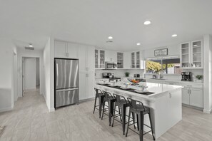 Une cuisine moderne avec des meubles blancs, des appareils en acier inoxydable et un  îlot central doté de tabourets de bar.