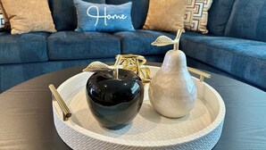 Una sala de estar moderna con un sofá azul oscuro, una bandeja decorativa con un jarrón negro, un jarrón blanco y un adorno dorado.