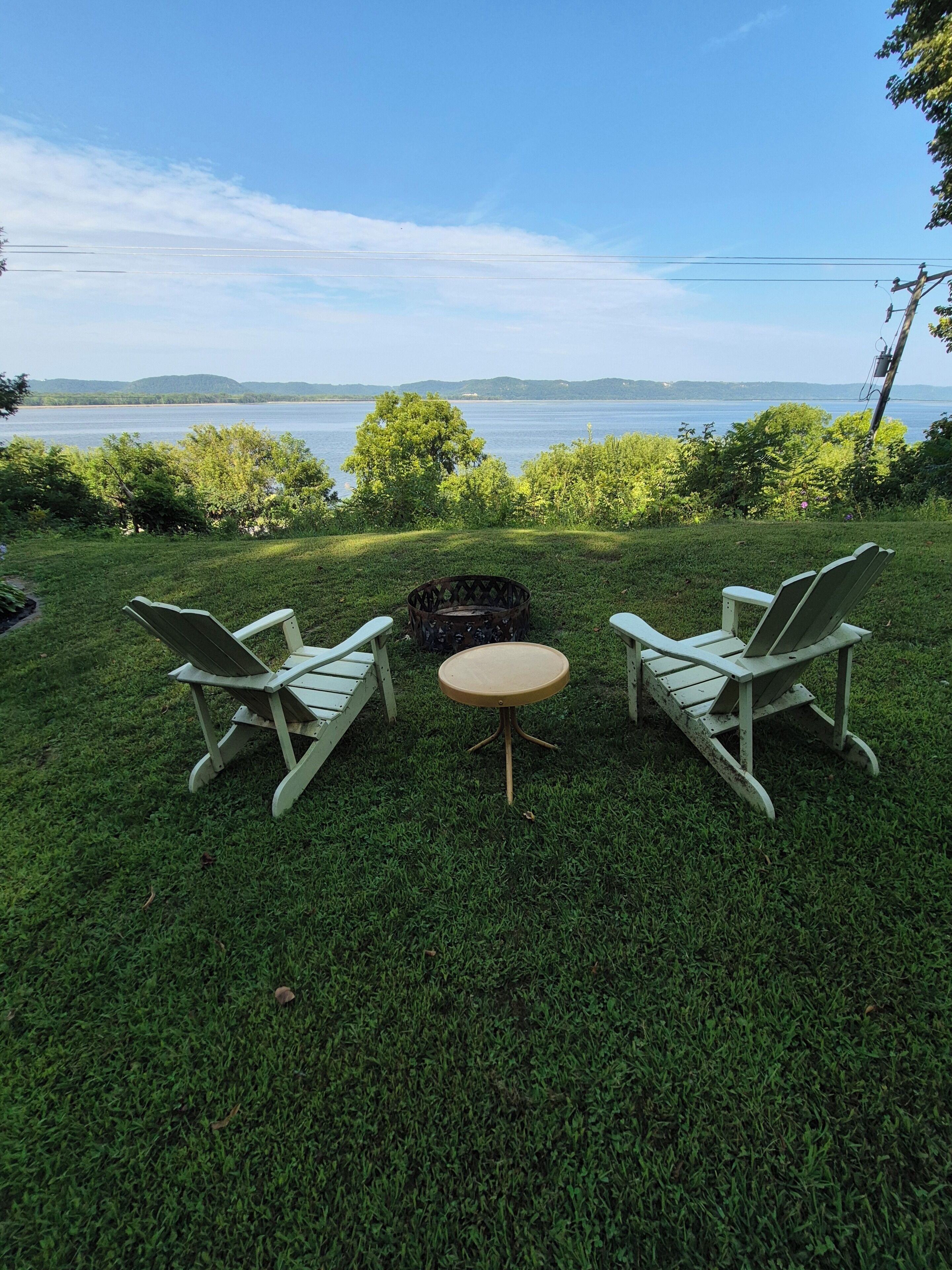 A grassy outdoor area with two Adirondack chairs and a small round table.
