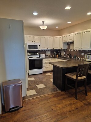 A kitchen with white cabinets, a microwave, stove, and a sink. There is a trash can and a wooden floor. - Enchanting 3-bedroom house with WiFi in Genoa (Genoa)