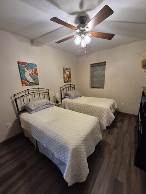 Une chambre avec deux lits, un ventilateur de plafond et deux tableaux accrochés au mur.
