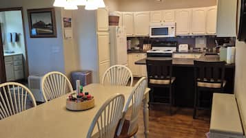 A modern kitchen with white cabinetry, a dining table with chairs, and a hanging light fixture.