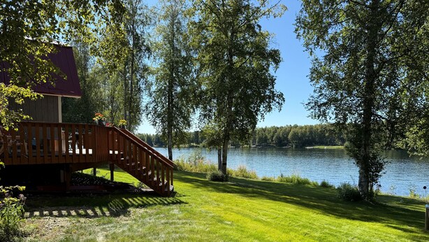 Una terraza de madera con una escalera que lleva a una casa junto a un lago.
