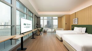Una habitación de hotel moderna con un ventanal grande, un escritorio, dos camas y una pared verde.