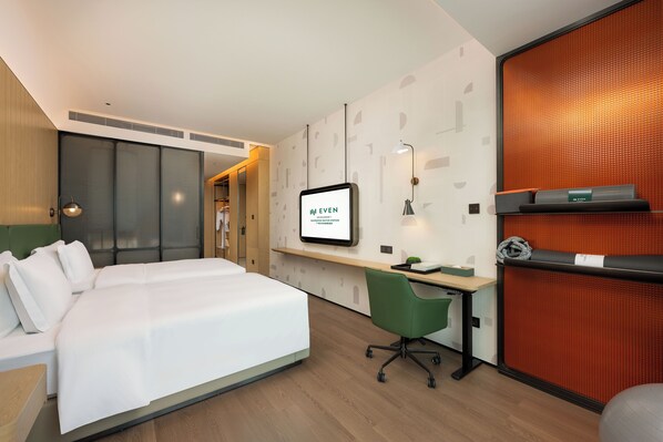 Una habitación de hotel moderna con una cama grande, un escritorio con una computadora, una silla de oficina verde y un televisor montado en la pared.