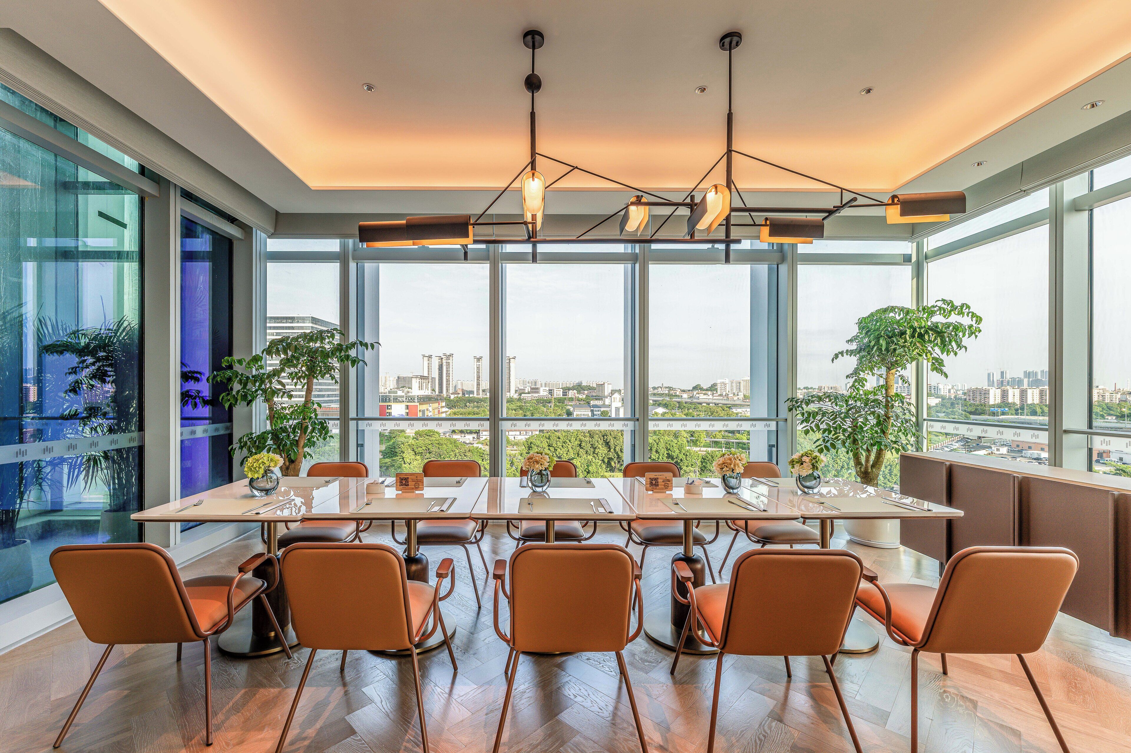 A modern meeting room with a large table, orange chairs, and large windows offering a city view.