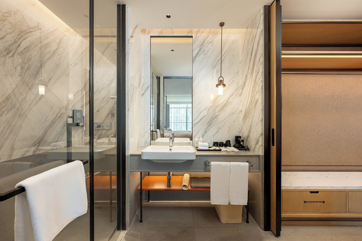 A modern bathroom with a glass-enclosed shower, a marble vanity, and a wooden cabinet.