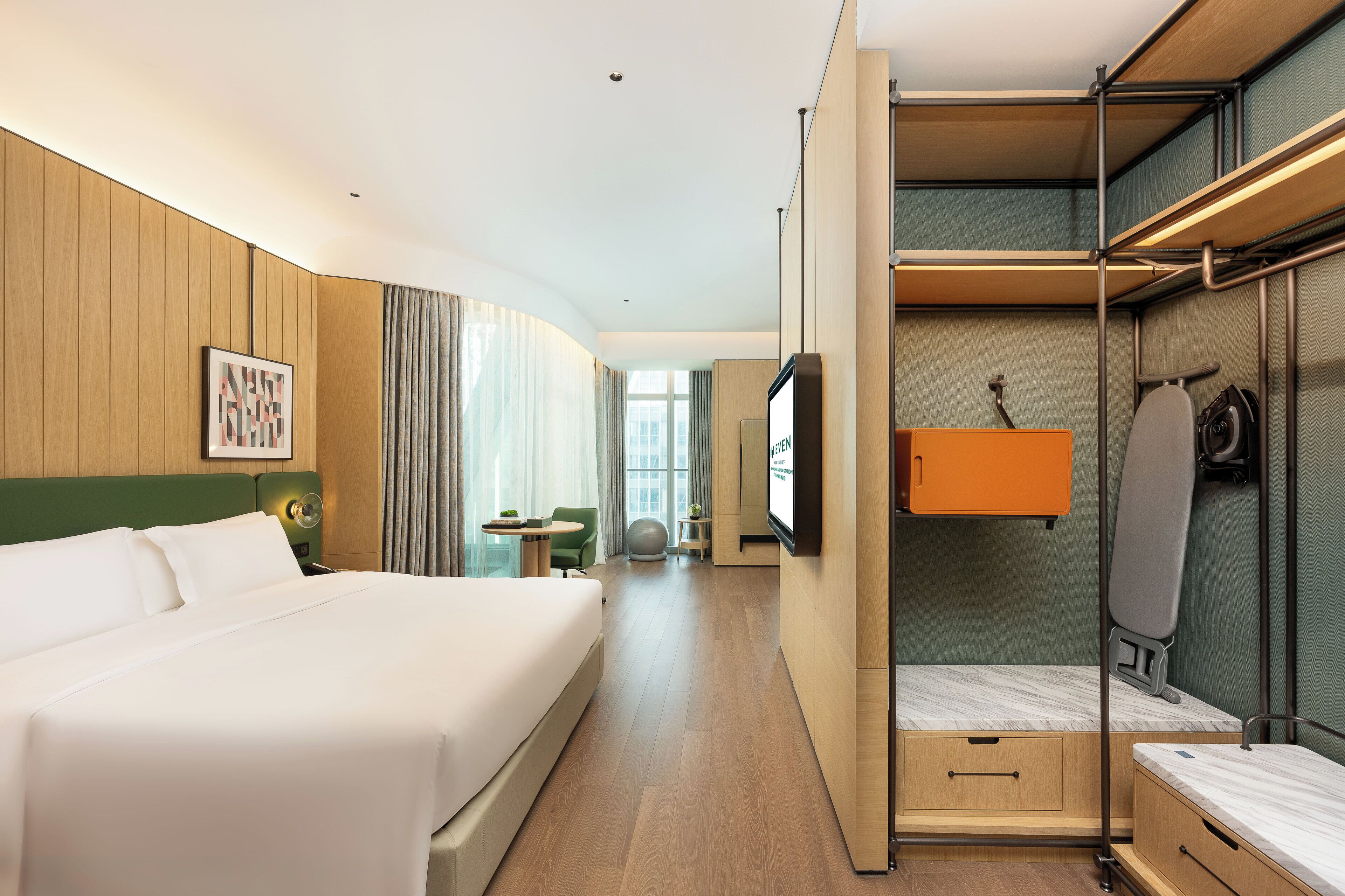 A hotel room with a large bed, a desk with a chair, a television, a wardrobe, and a mirror.
