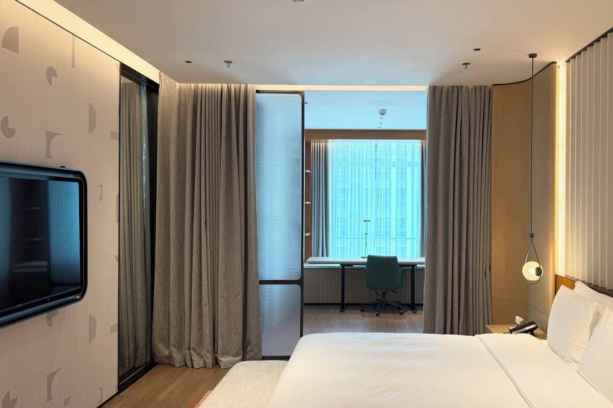 Habitación de hotel con una cama grande, un escritorio con silla, un televisor y una ventana con cortinas.