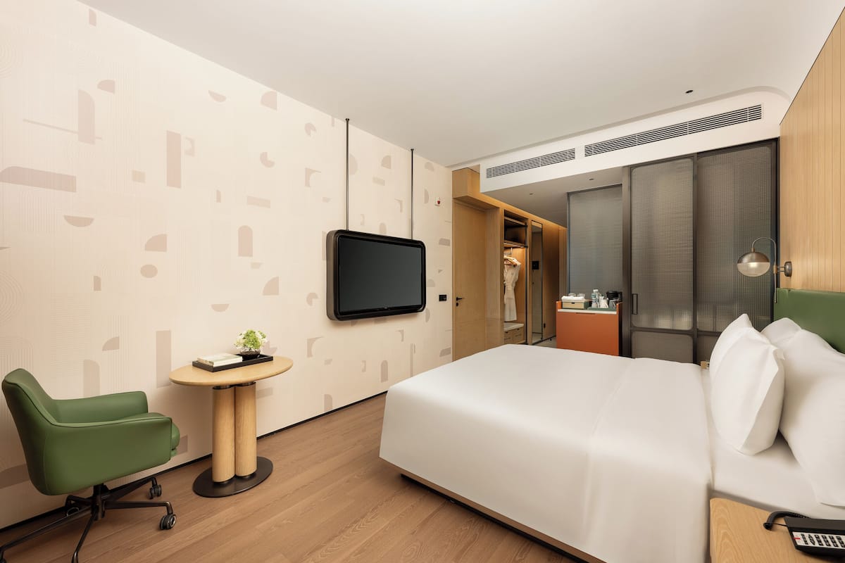 Una habitación de hotel con cama, escritorio, silla, televisor y armario.